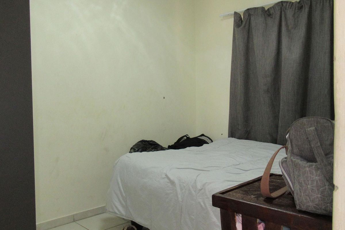 A bedroom featuring tiled flooring and a curtain rail, currently showing signs of wear on the walls.