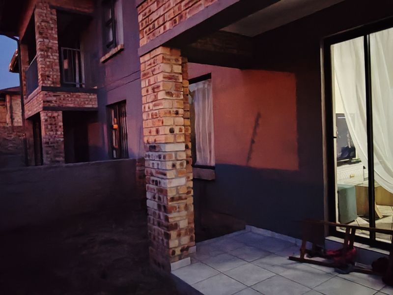 A covered patio area featuring exposed brick columns and tiled flooring, providing direct access to the interior through sliding glass doors.