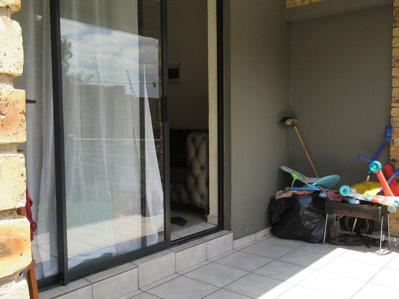 A covered patio area featuring tiled flooring and face brick pillars, providing direct access to the interior through a sliding glass door.