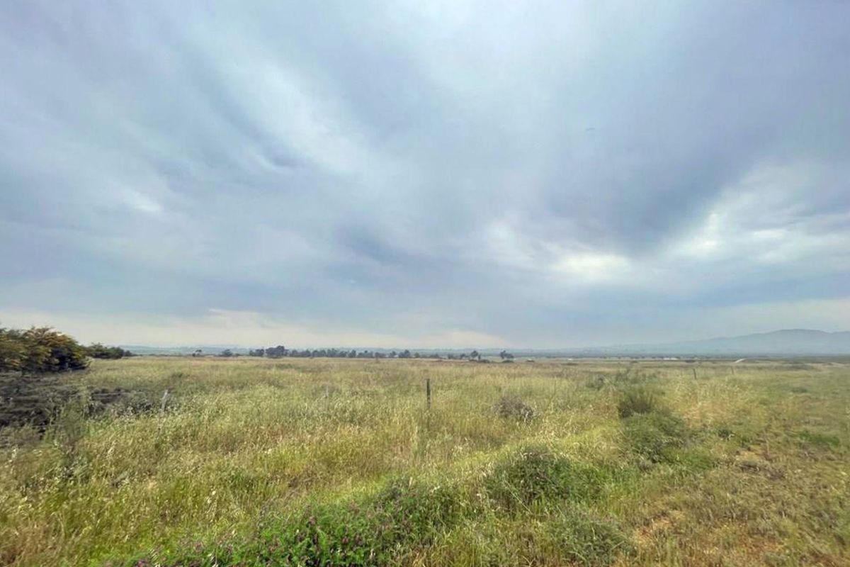 A wide-angle view of the vacant residential land, featuring natural grass terrain and perimeter wire fencing under an overcast sky.
