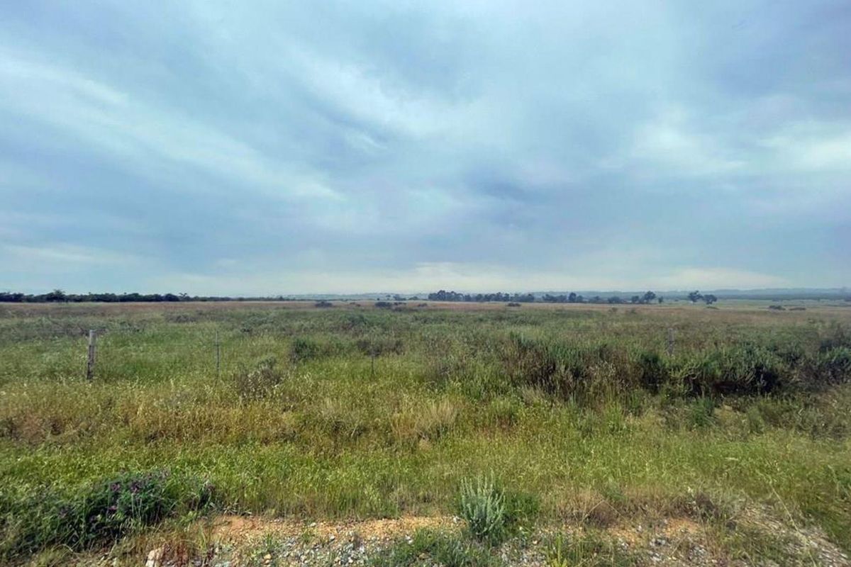 A wide, open expanse of vacant residential land featuring natural grass coverage and perimeter wire fencing.