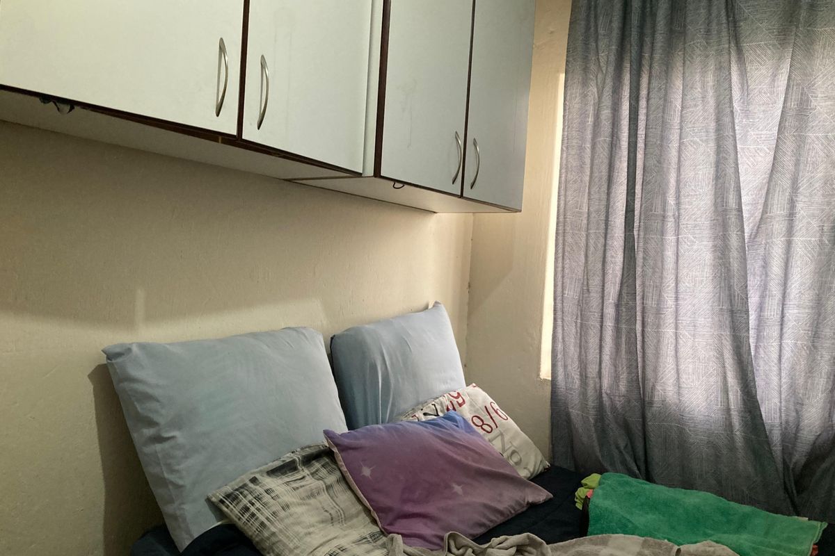 A bedroom featuring built-in overhead storage cabinetry and a window with curtains.