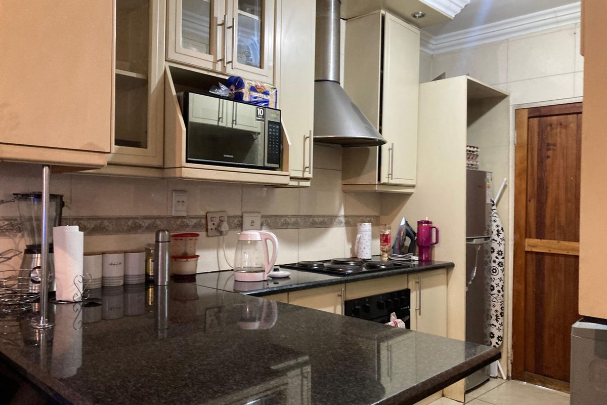 A functional kitchen featuring granite countertops, built-in cabinetry, an electric hob with extractor fan, and tiled finishes throughout.