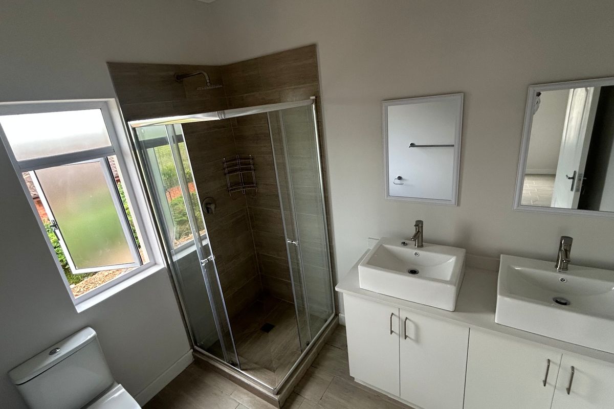 Modern bathroom featuring a double vanity with vessel sinks, a glass-enclosed shower with tiled walls, and a toilet.