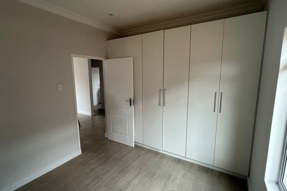 A clean, empty bedroom featuring modern tiled flooring, white built-in cupboards, and a classic tongue and groove ceiling.