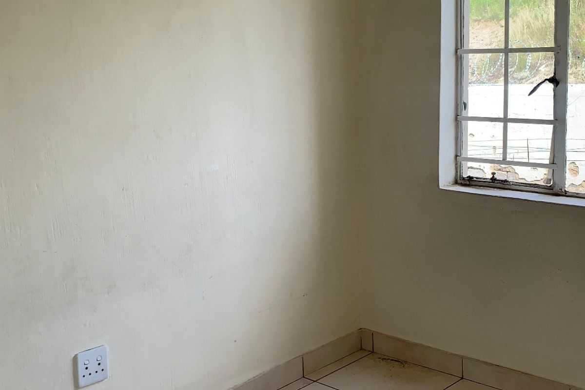 An empty bedroom featuring tiled flooring, a window with security bars, and neutral wall finishes, ready for a fresh update.