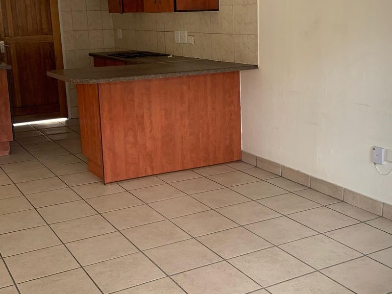 A functional kitchen area featuring built-in wooden cabinetry, a breakfast bar, tiled flooring, and a tiled backsplash, offering a blank canvas for updates.