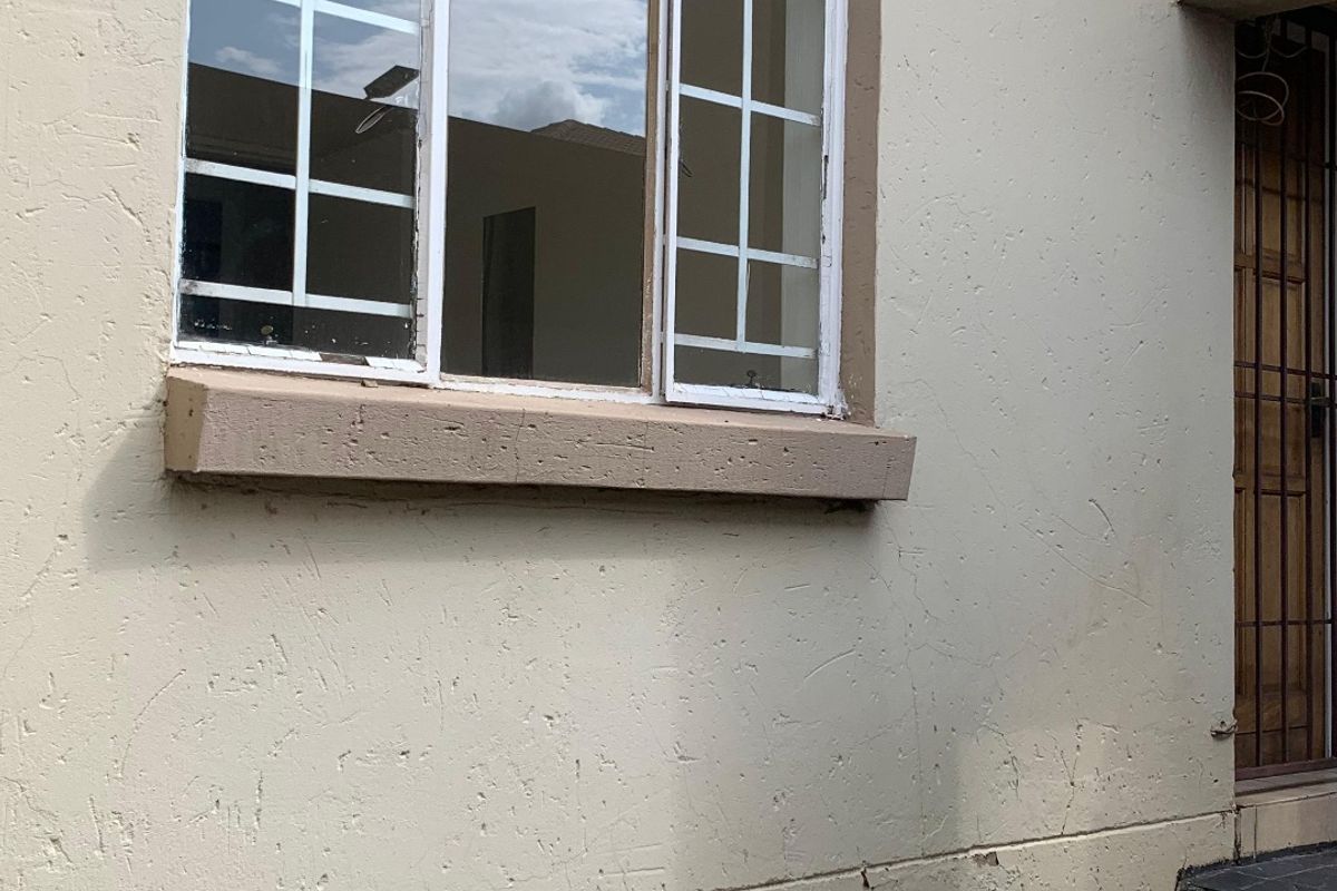 Exterior view of the property showing a window, security gate, tiled steps, and paved area with visible signs of wear and weathering.