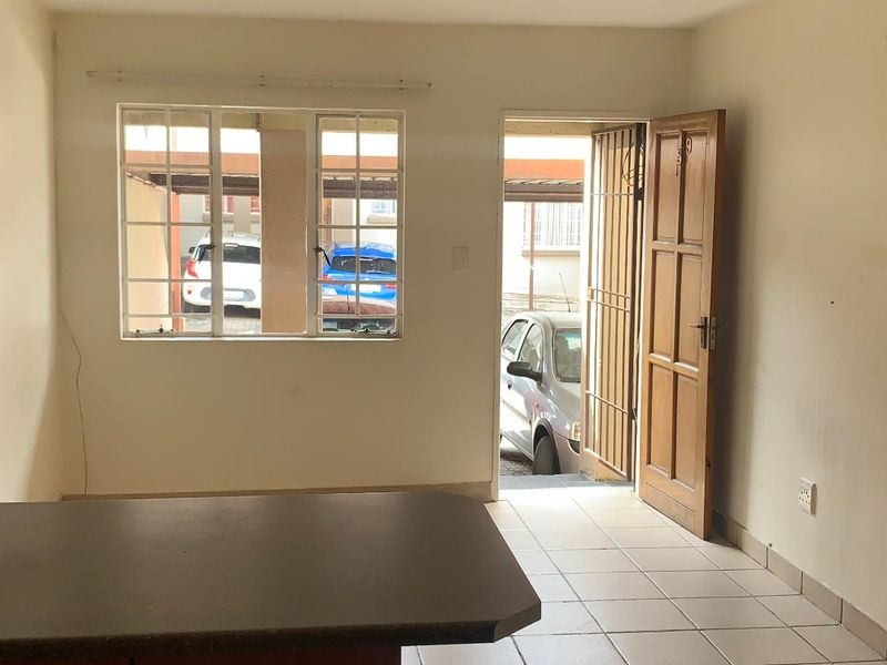 Open-plan living area featuring tiled flooring, a kitchen island with built-in cabinetry, and direct access to the exterior through a security gate.