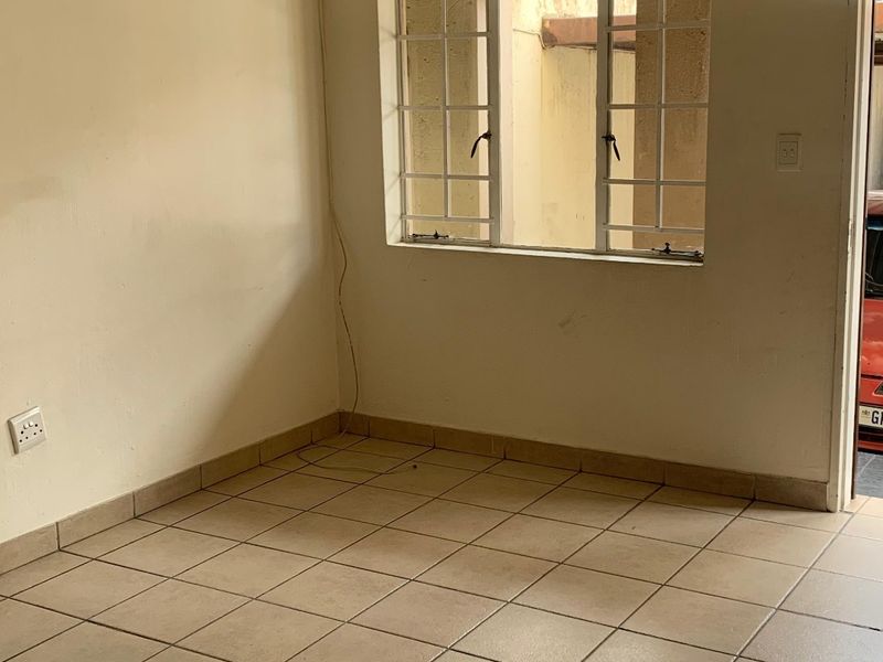 An empty living area featuring neutral ceramic floor tiles, a ceiling-mounted spotlight, and a window with security bars.
