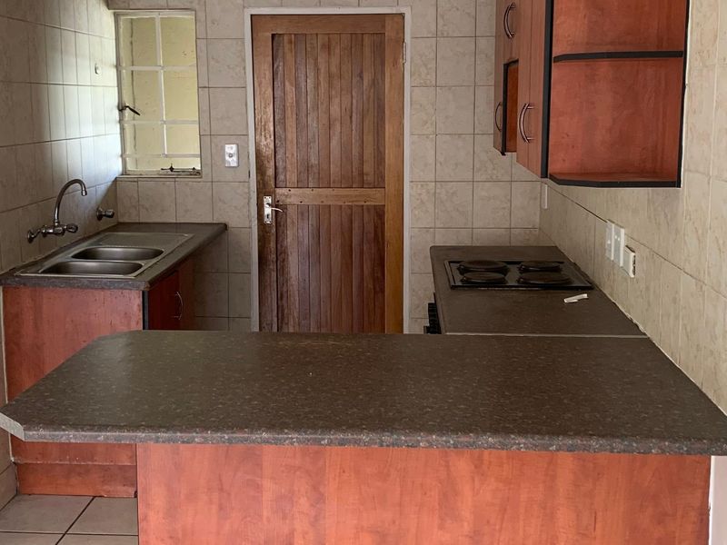 A dated kitchen featuring laminate cabinetry, stone-look countertops, a built-in hob, and a double bowl sink with ceramic wall and floor tiling.