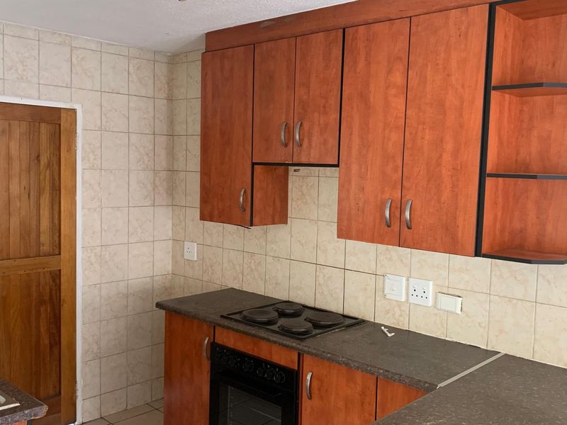 A functional kitchen featuring wood-look cabinetry, dark laminate countertops, a built-in oven and hob, and a double sink with tiled splashbacks.