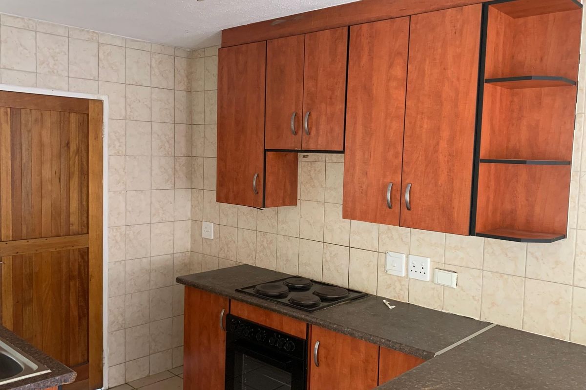 A functional kitchen featuring wood-look cabinetry, dark laminate countertops, a built-in oven and hob, and a double sink with tiled splashbacks.