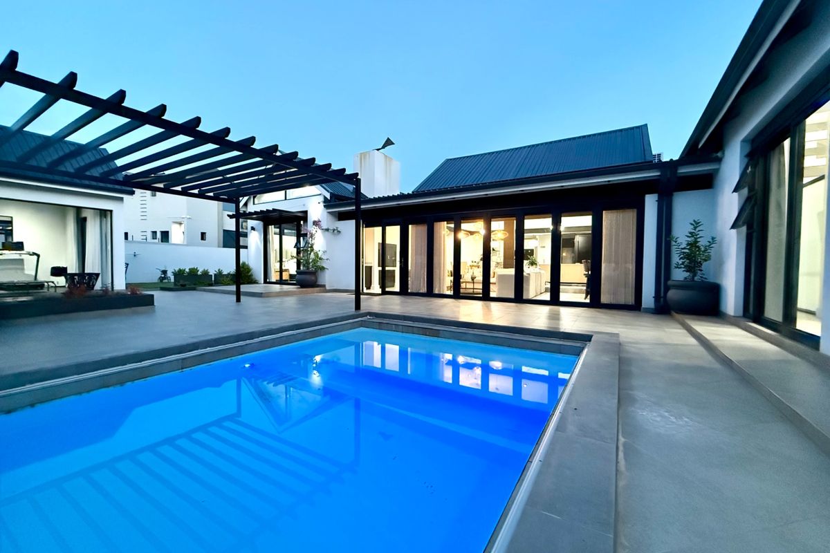 A modern outdoor entertainment area featuring a swimming pool, a timber pergola, and large sliding glass doors leading into the home.