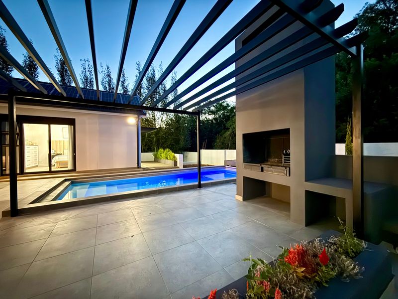 Modern outdoor entertainment area featuring a swimming pool, a sleek pergola, and a built-in braai, perfect for alfresco dining and relaxation.