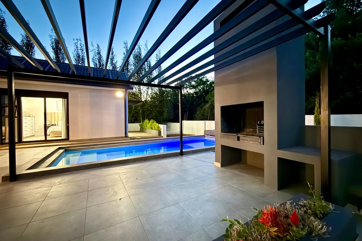 Modern outdoor entertainment area featuring a swimming pool, a sleek pergola, and a built-in braai, perfect for alfresco dining and relaxation.