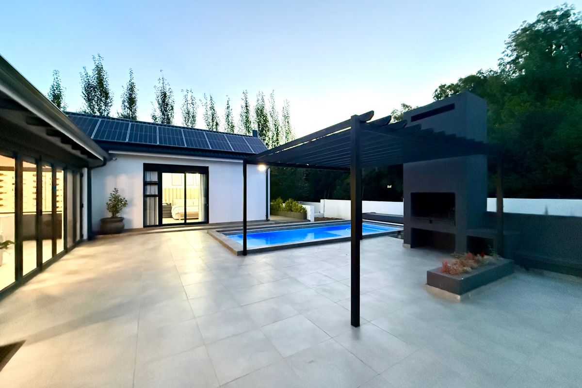 Modern outdoor entertainment area featuring a swimming pool, a covered pergola with a built-in braai, and large sliding doors leading to the interior.