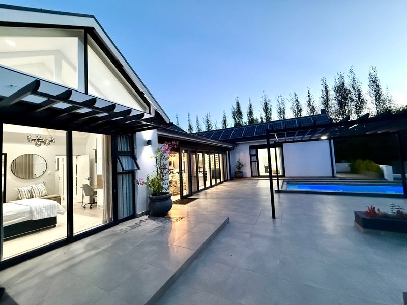 Modern rear exterior featuring a spacious tiled patio, swimming pool, pergola, and large glass sliding doors connecting to the interior living spaces.