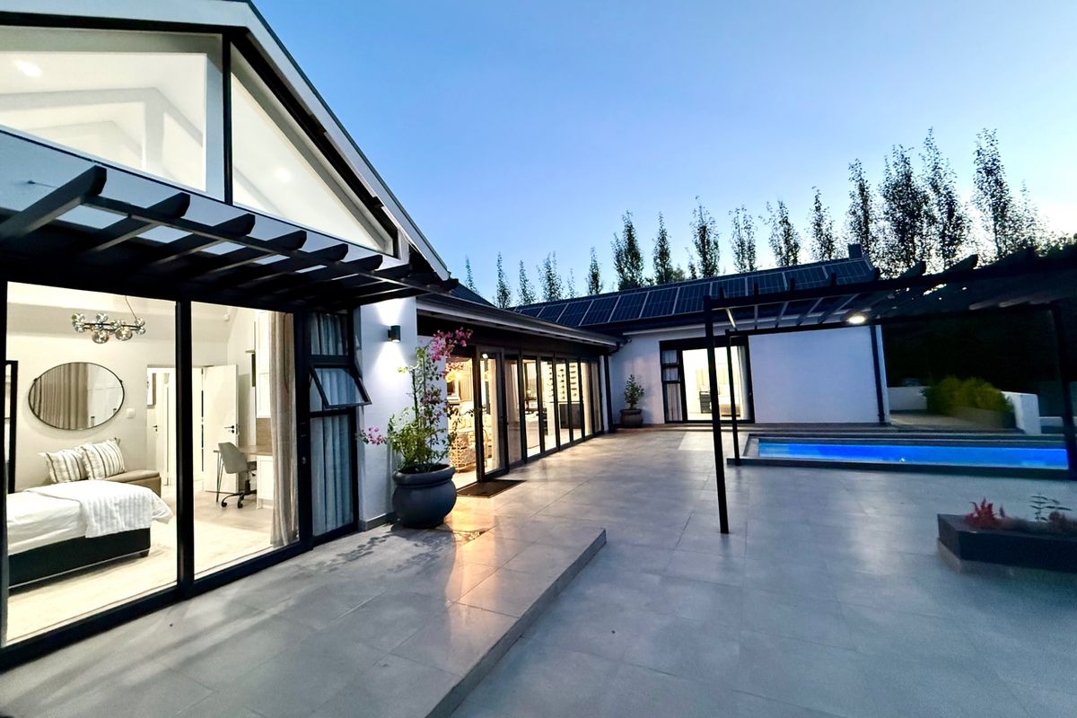 Modern rear exterior featuring a spacious tiled patio, swimming pool, pergola, and large glass sliding doors connecting to the interior living spaces.