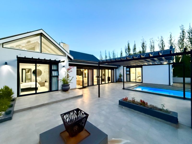 A modern rear courtyard featuring a tiled patio, swimming pool, and pergola, seamlessly connecting to the interior living spaces through large sliding glass doors.