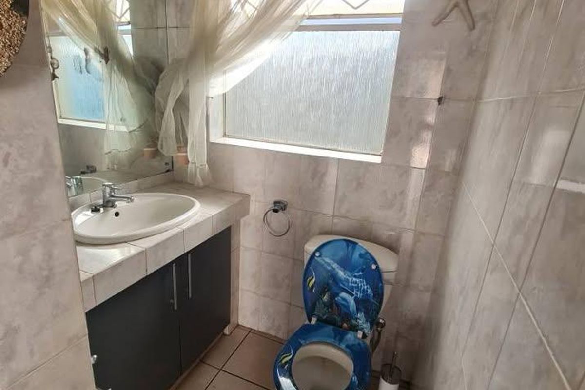 A compact bathroom featuring tiled walls and flooring, a vanity cabinet with a basin, and a window with obscured glass.