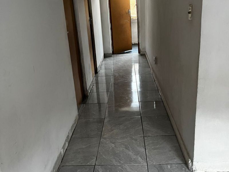 A narrow hallway featuring grey tiled flooring and multiple internal doors, requiring minor cosmetic finishing to the skirting boards and walls.