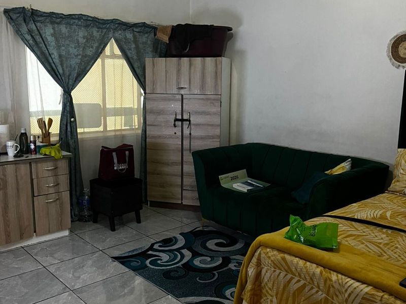 A bedroom featuring tiled flooring and a window with security bars, offering a functional living space with potential for cosmetic updates.