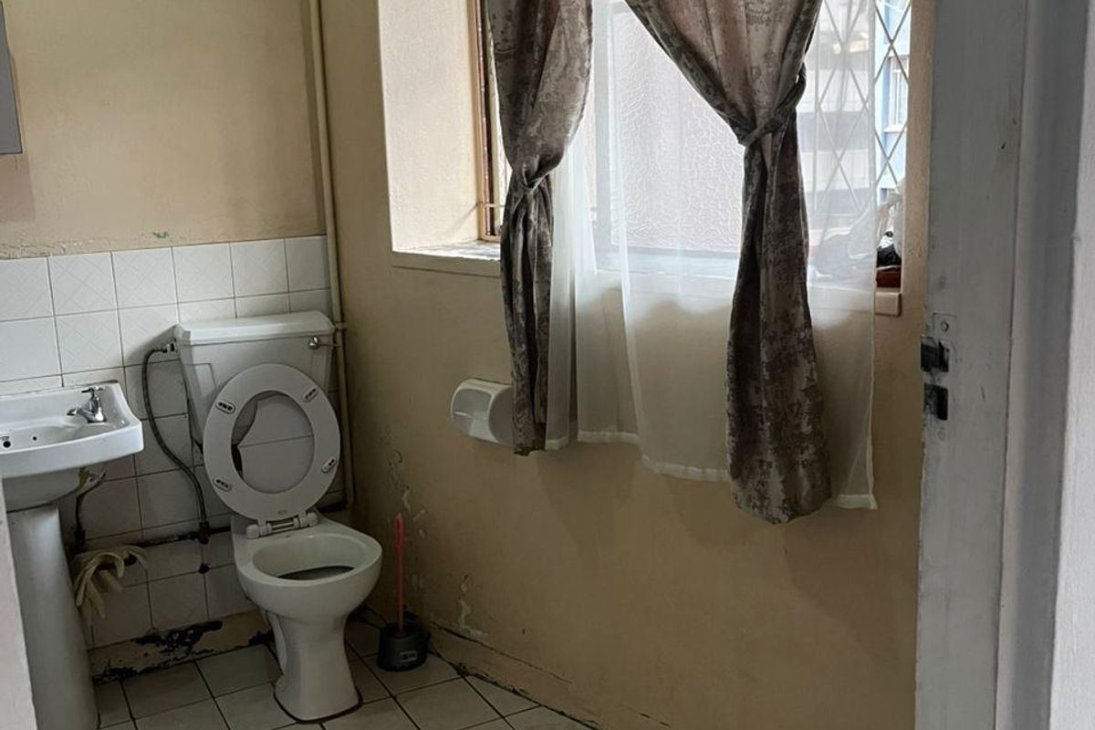 A dated bathroom featuring a pedestal basin and toilet, requiring significant cosmetic renovation and repair to wall finishes and flooring.