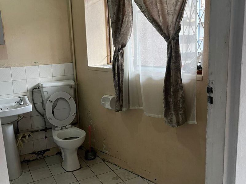 A dated bathroom featuring a pedestal basin and toilet, requiring significant cosmetic renovation and repair to wall finishes and flooring.