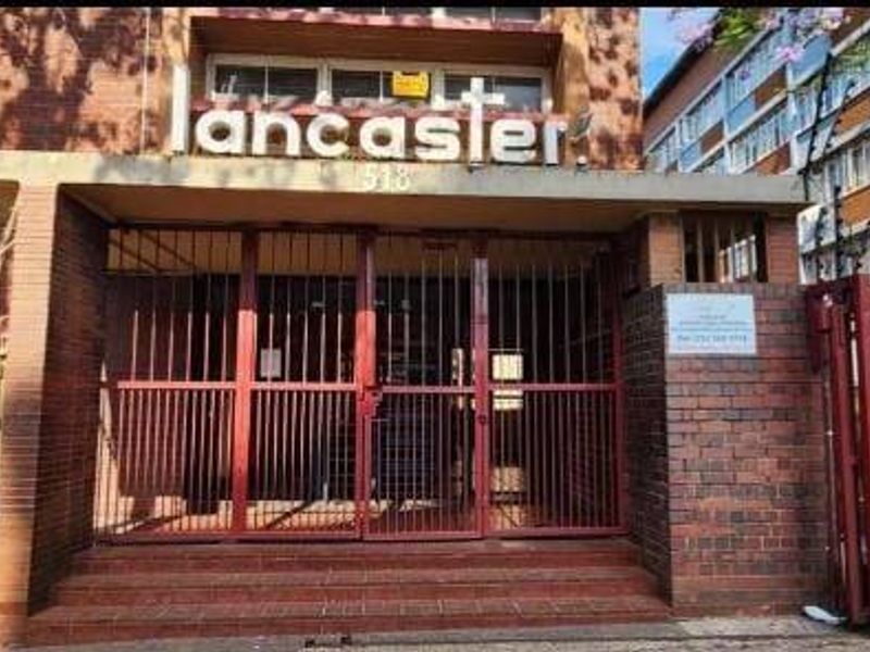 Front entrance of the Lancaster apartment building featuring brick facade, secure gated access, and perimeter electric fencing.
