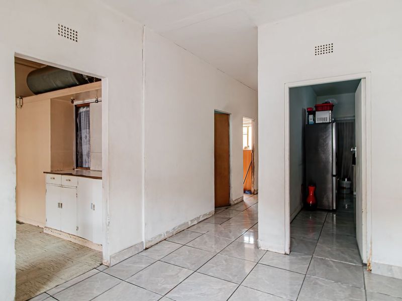 A tiled hallway providing access to adjacent rooms, featuring neutral walls and ventilation grilles, requiring minor cosmetic updates to improve overall presentation.