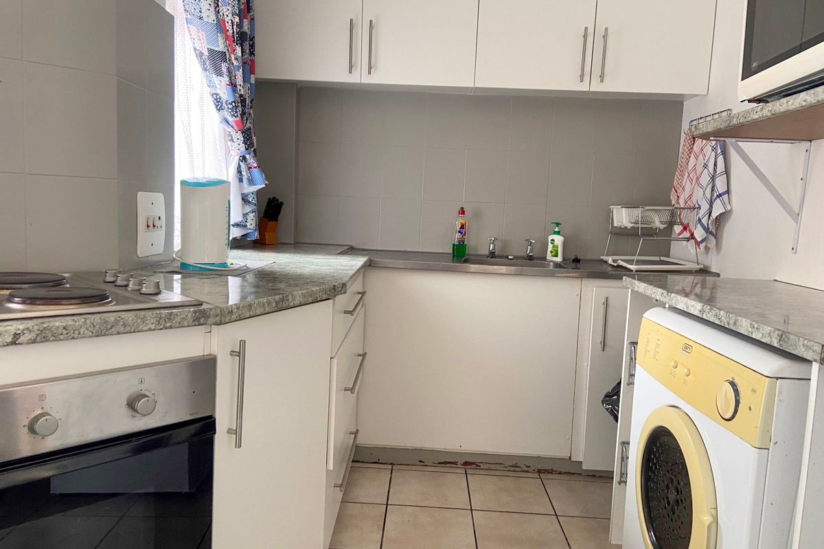 Compact kitchen featuring white cabinetry, laminate countertops, tiled backsplash, and built-in oven and hob, with tiled flooring throughout.