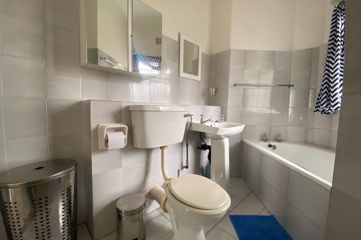 A functional bathroom featuring a pedestal washbasin, toilet, and bathtub with neutral wall tiling and a wall-mounted medicine cabinet.