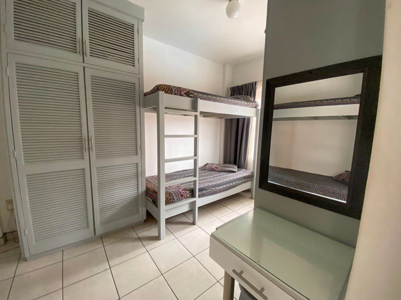 A functional bedroom featuring a built-in wardrobe with louvered doors and tiled flooring, providing practical storage and living space.
