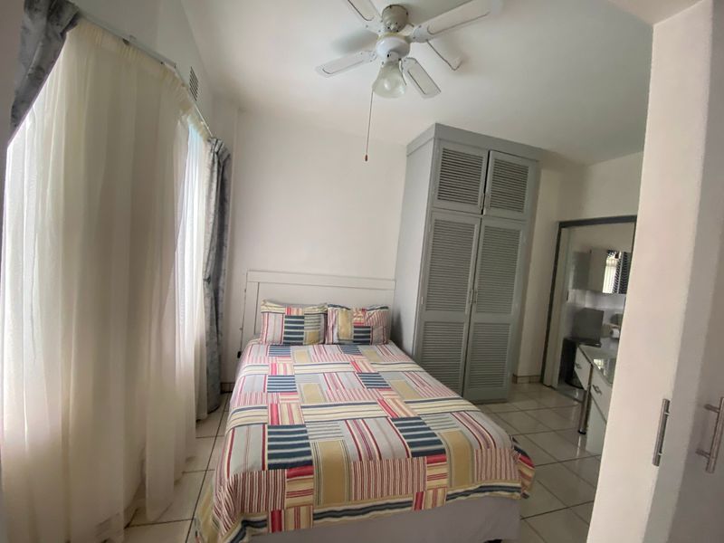 A bedroom featuring tiled flooring, a ceiling fan, and a built-in wardrobe with louvered doors.
