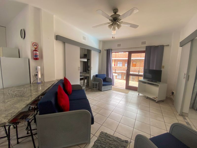 Open-plan living area featuring tiled flooring, a ceiling fan, and a sliding door providing access to an outdoor balcony space.
