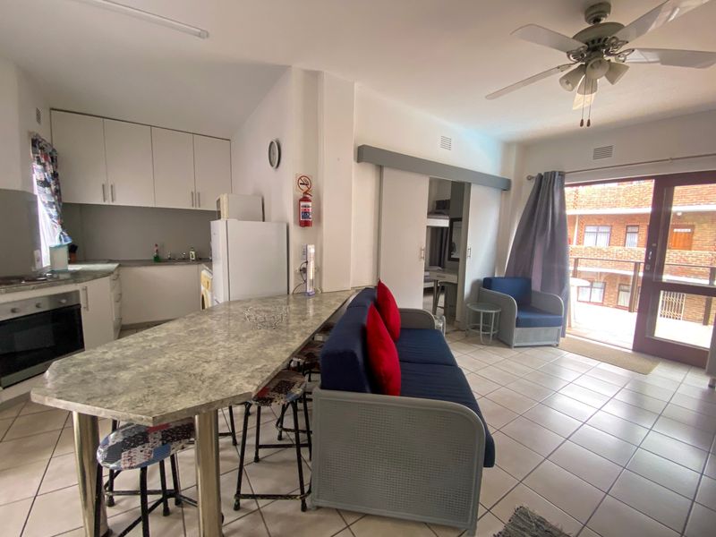 Open-plan apartment living area featuring a functional kitchen with built-in cabinetry, breakfast bar, and direct access to a balcony through a sliding door.