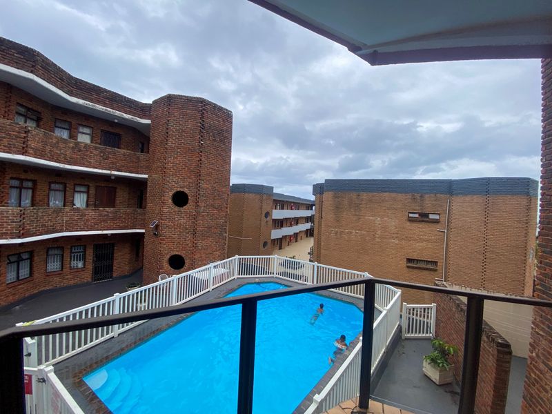 View from a balcony overlooking a communal swimming pool area surrounded by brick apartment buildings.