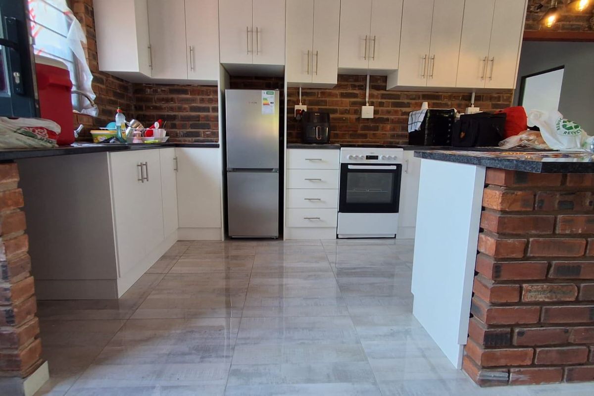 A modern kitchen featuring white cabinetry, exposed brick accents, tiled flooring, and a functional island with a stone countertop.