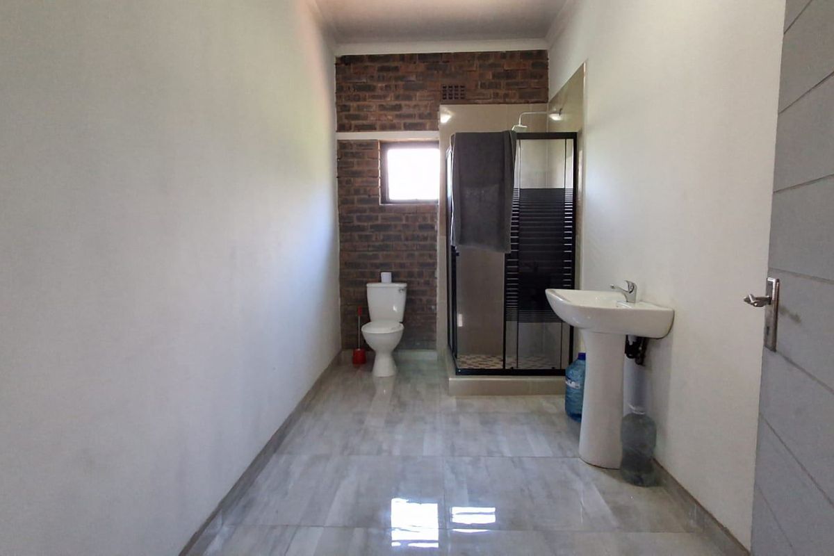 A clean, modern bathroom featuring a pedestal basin, toilet, and a glass-enclosed shower with an exposed brick feature wall.