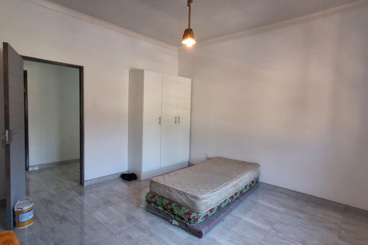 A simple bedroom featuring tiled flooring, a built-in wardrobe, and a central pendant light fixture.