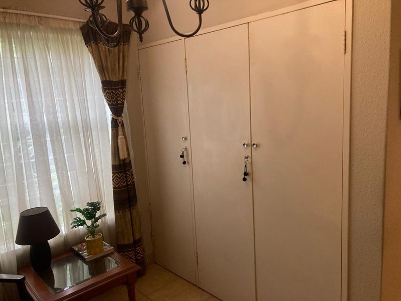 A bedroom featuring built-in cupboards with tiled flooring and natural light from the adjacent window.