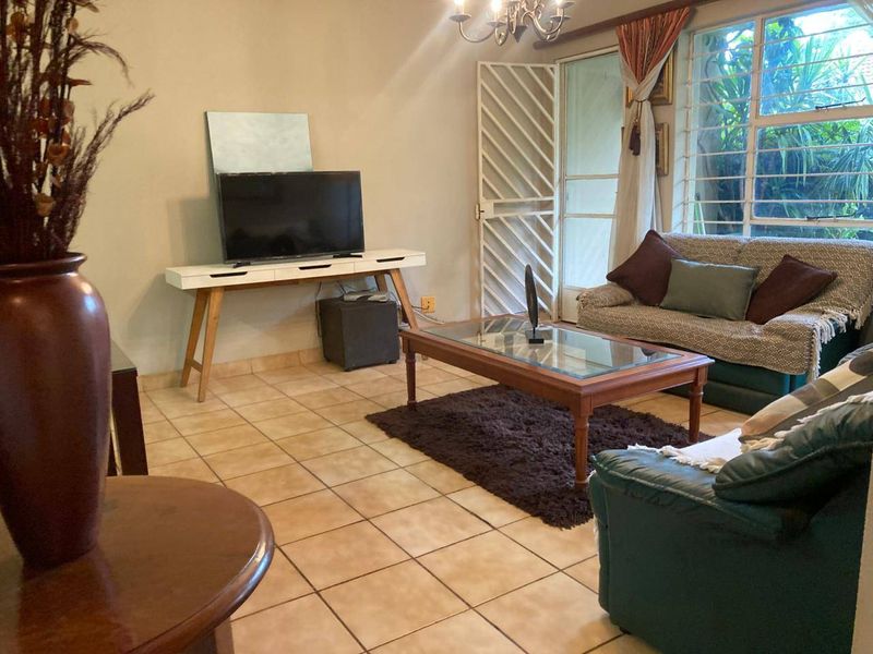 A comfortable living room featuring tiled flooring, a large window for natural light, and a security gate leading to the outdoor area.