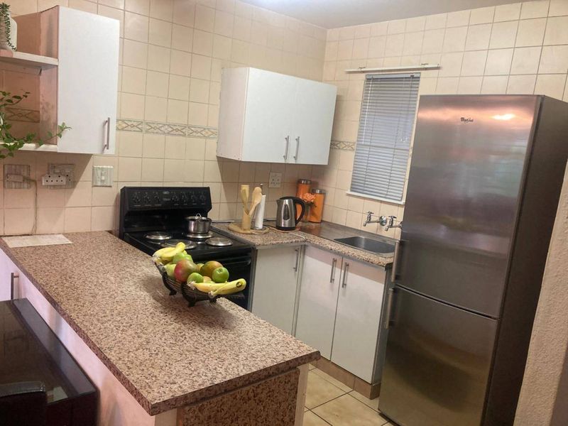 A functional kitchen featuring laminate countertops, tiled backsplash, built-in cabinetry, and a stainless steel sink, offering a practical layout for daily meal preparation.