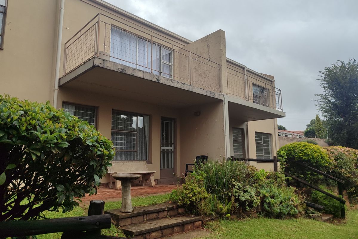 Rear view of the apartment building featuring a ground floor patio, upper level balcony with metal railings, and established garden area.