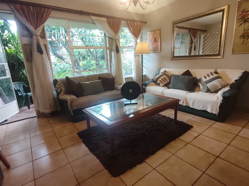 A comfortable living room featuring tiled flooring, large windows with security bars, and direct access to an outdoor patio area.