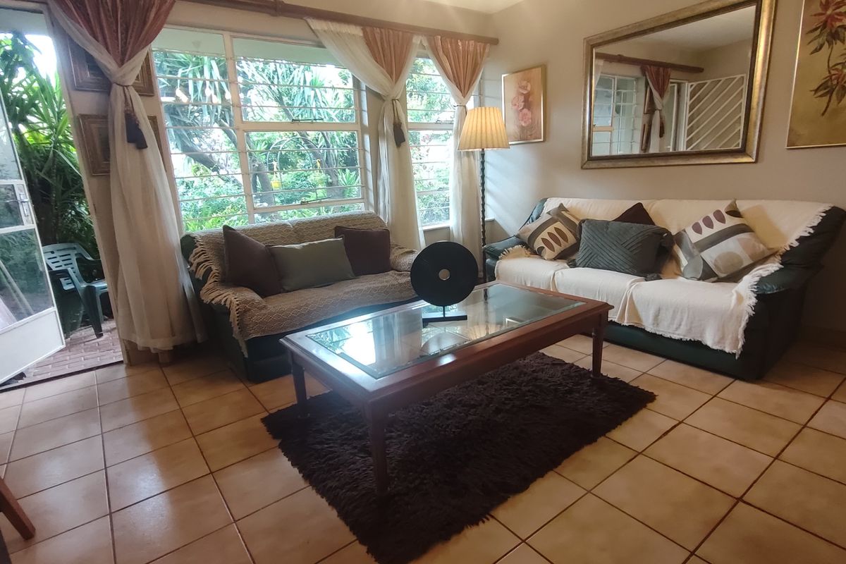 A comfortable living room featuring tiled flooring, large windows with security bars, and direct access to an outdoor patio area.