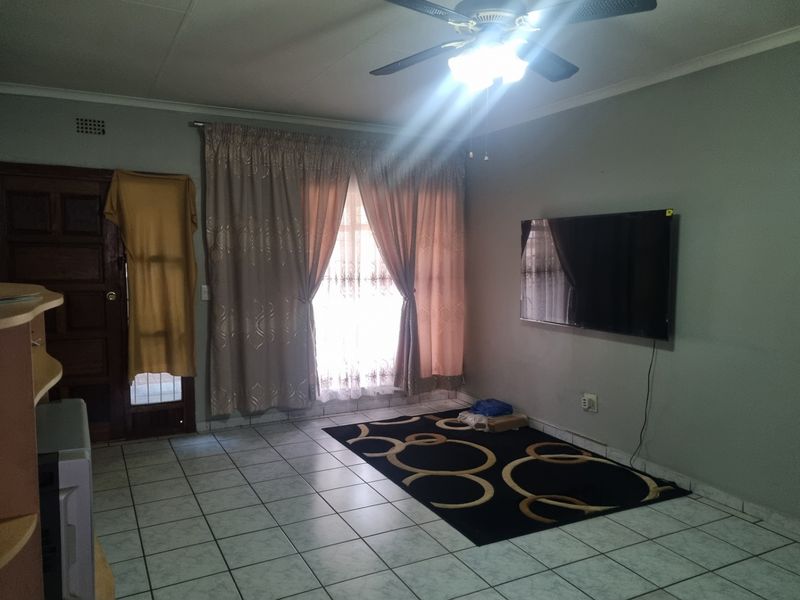 A spacious living room featuring tiled flooring, a ceiling fan, and a timber door, offering a neutral canvas for personalization.