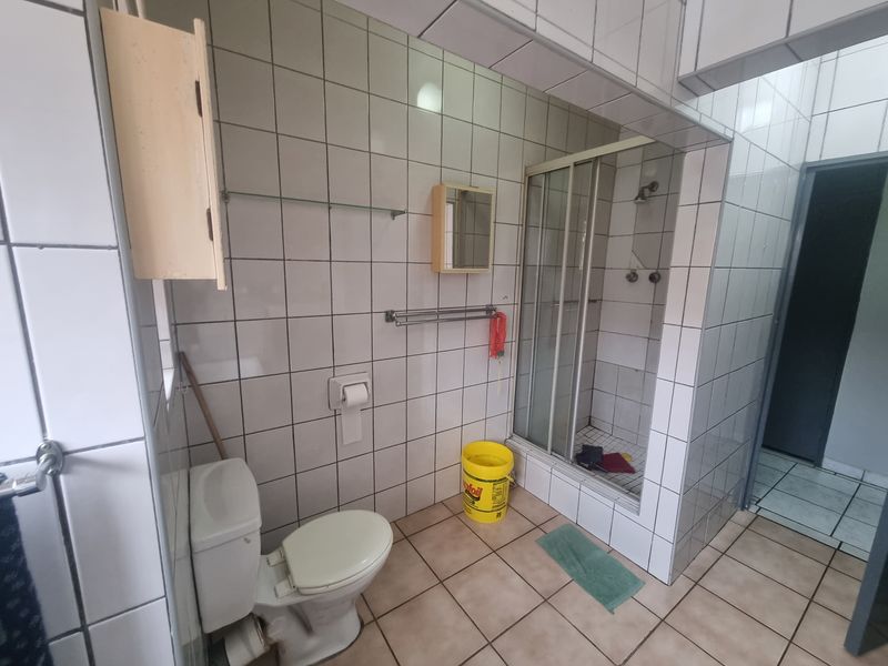 A dated bathroom featuring a shower enclosure, toilet, and tiled finishes. The space requires renovation to update the fixtures and finishes.