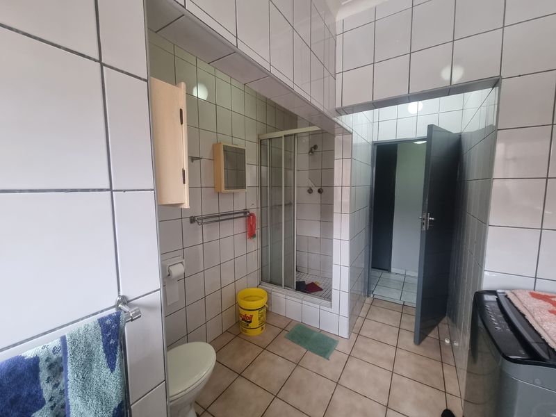 A functional bathroom featuring a shower enclosure, tiled walls and flooring, and standard sanitary fixtures, requiring cosmetic updates to improve its overall condition.